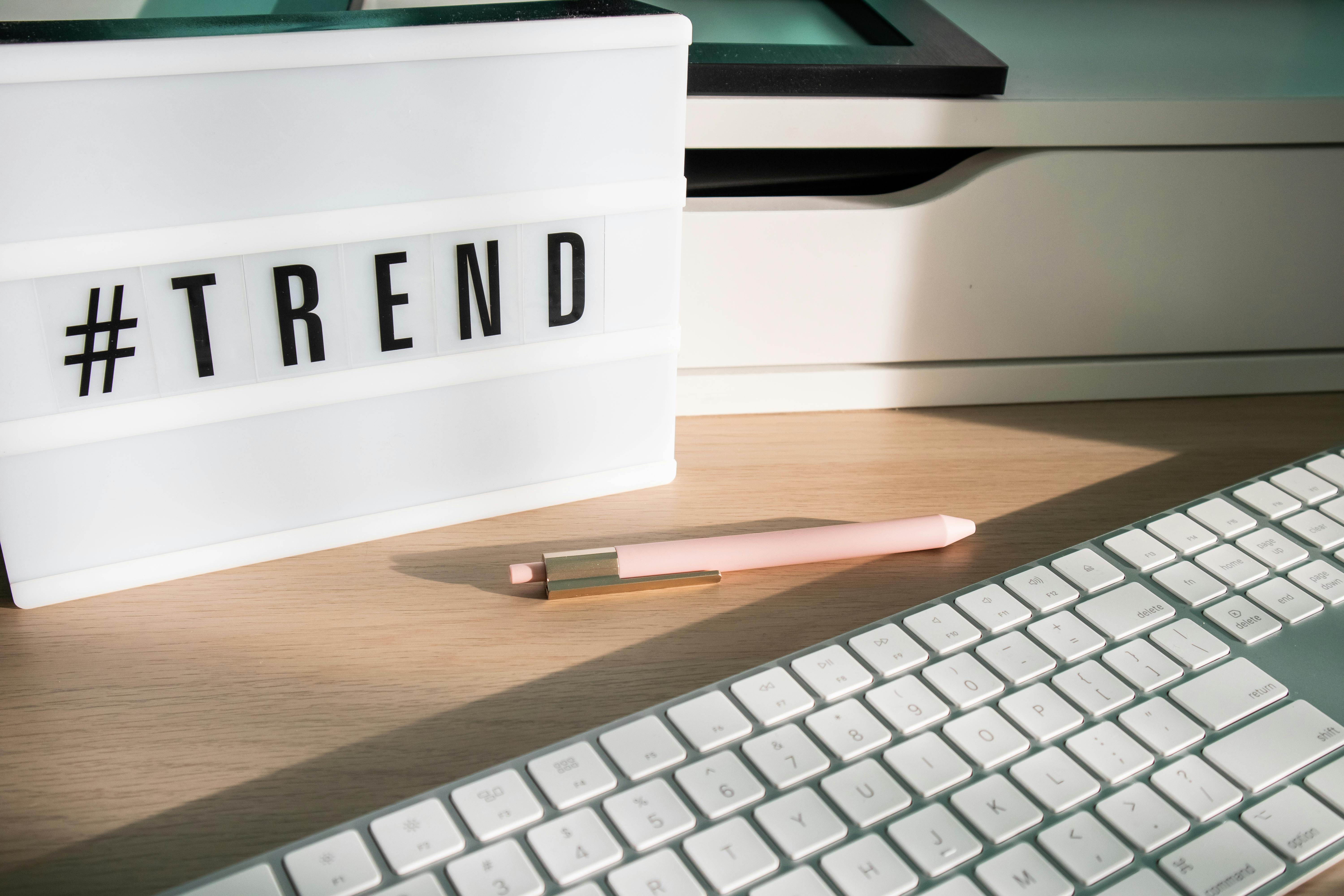 Close-up of a white lightbox with the word hashtag trend beside a keyboard, symbolizing digital trend culture