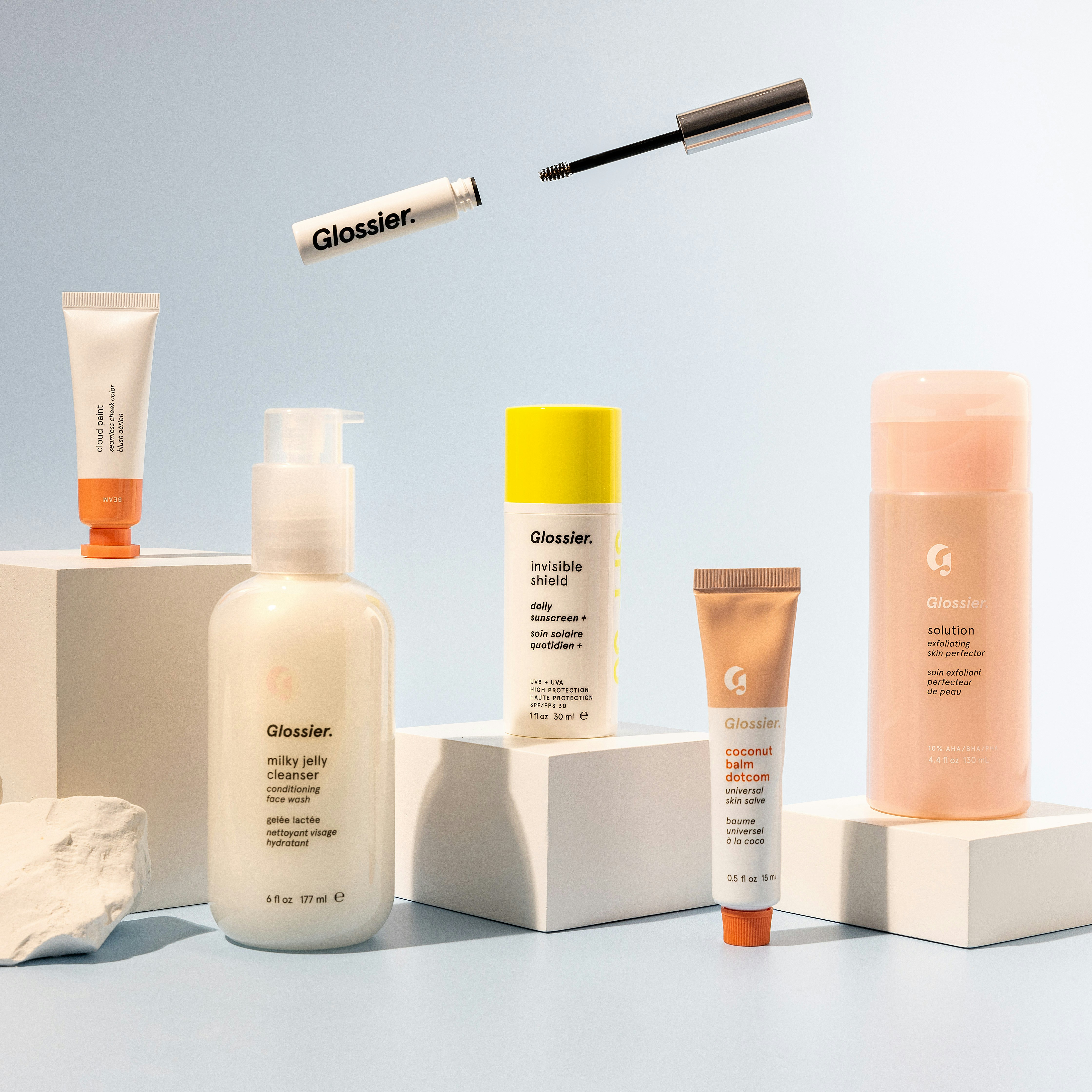 Assorted Glossier skincare and makeup products displayed on minimalist pedestals, representing aesthetic branding.