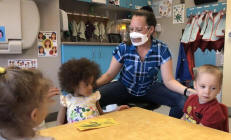 Daycare worker with children during COVID-19 precautions.