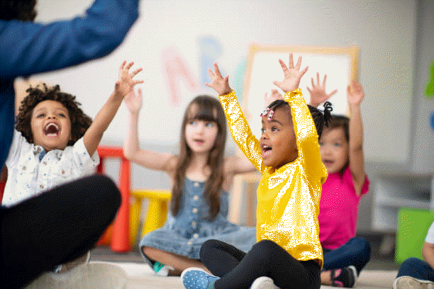 Preschool students sitting with their legs crossed on the floor in the classroom.